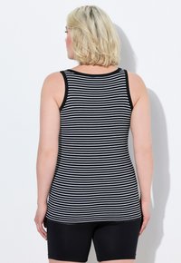 Top a righe bianche e nere con scollatura a girocollo e design aderente, abbinato a pantaloni corti neri uniti, visto da dietro.