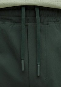 Dunkelgrüne Sportshorts aus strukturiertem Material, mit elastischem Bund und passenden Kordeln mit abgerundeten Spitzen, von oben präsentiert.