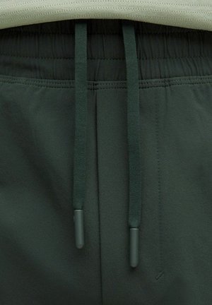 Pantaloni sportivi verdi scuri con tessuto testurizzato, vita elastica e coulisse abbinate con punte arrotondate, mostrati dall'alto.