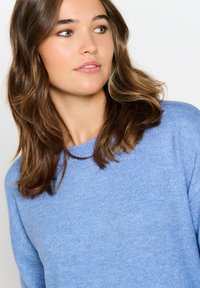 Maglione azzurro chiaro con lavorazione a maglia testurizzata, scollo tondo e maniche lunghe. Il tessuto sembra morbido e confortevole su uno sfondo neutro.
