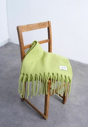 Hellgrüner, fransiger Schal mit einem Topshop-Label, der über die Rückenlehne eines abgenutzten Holzstuhls auf einem grauen Boden drapiert ist.