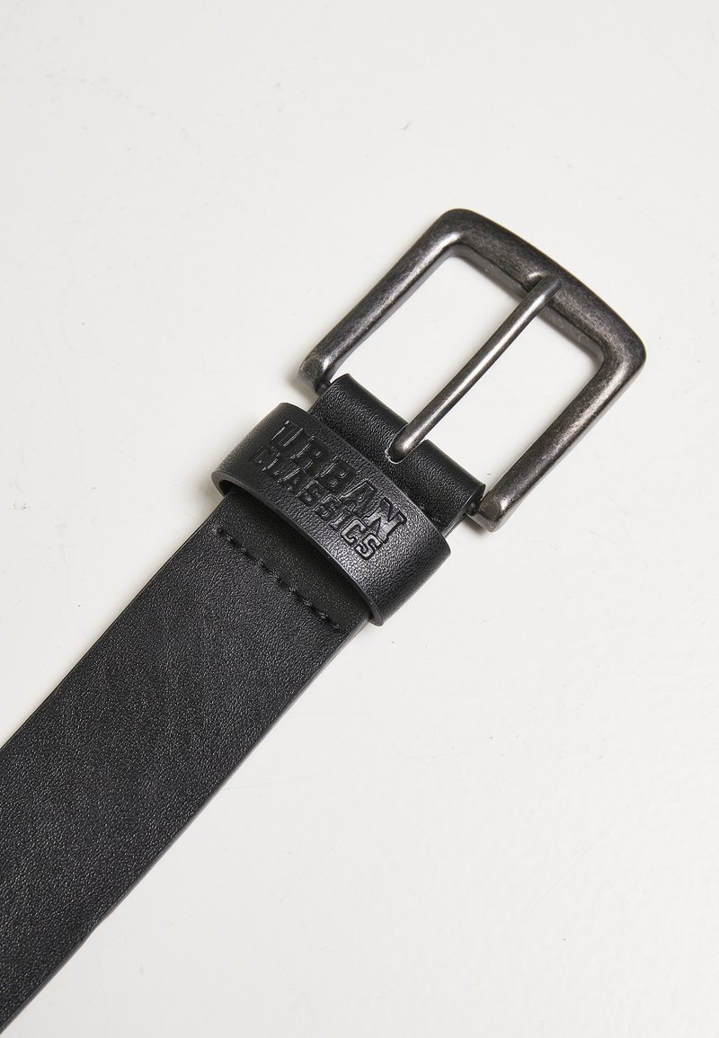 Schwarzer Leder Gürtel mit einer Metall-Schnalle mit gebürsteter Oberfläche. Der Riemen hat eine strukturierte Oberfläche und ein geprägtes Logo.