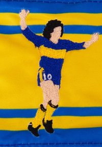 Geborduurd patch met een speler in een blauw en gele uniform, met het nummer 10, afgebeeld in een feestelijke pose tegen een gestreepte achtergrond.