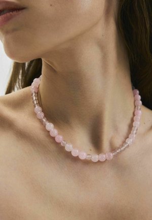 Prim-plan cu gâtul unei persoane care poartă un colier cu mărgele rotunde, translucide, roz și transparente.