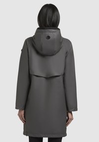 Grijze waterdichte jas met capuchon, met een ontspannen pasvorm, lange mouwen en een uitlopende achterzijde. Gladde textuur met minimale hardware.