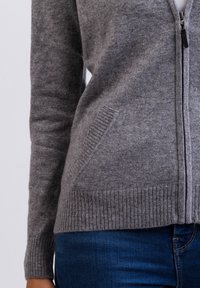 Grau gestrickte Strickjacke mit Reißverschluss, verfügt über gerippte Bündchen und Saum, seitliche Taschen und eine weiche Textur. Eignet sich für Lagenlooks.
