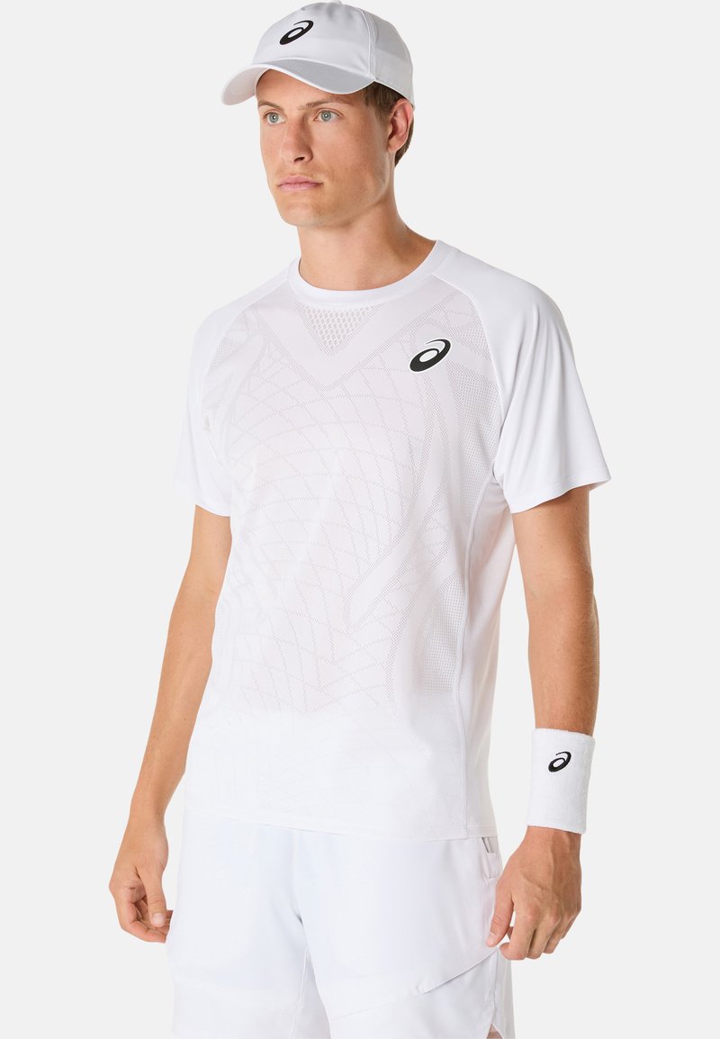 T-shirt atletica bianca con texture in rete e motivo geometrico, abbinata a un cappellino bianco e a un braccialetto coordinato, caratterizzati da un logo nero.