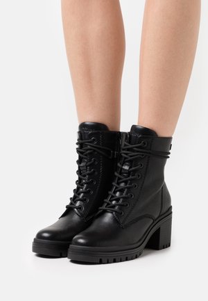 Botas de tobillo de cuero negro con cordones en la parte delantera, cremallera lateral, tacón chunky, superficie texturizada y suela robusta para mayor tracción.
