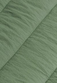 Gros plan sur un tissu vert avec des coutures diagonales et une texture légèrement froissée.