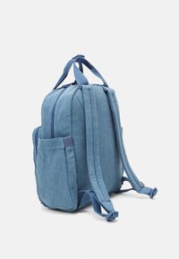 Mochila de tela azul con panel trasero acolchado, correas ajustables y bolsillos laterales. Presenta una forma estructurada y un compartimento principal con cremallera.