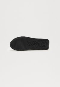 Black sneaker sole with textured grip patterns and embossed "HUGO" logo. Material appears rubber with a flat, rounded design.