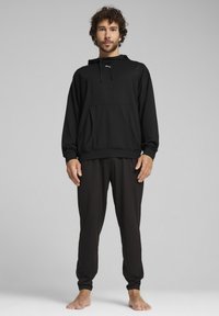 Haut à capuche noir avec cordon de serrage et poche avant, associé à un pantalon noir ajusté. Tissu doux et lisse avec une coupe ajustée.