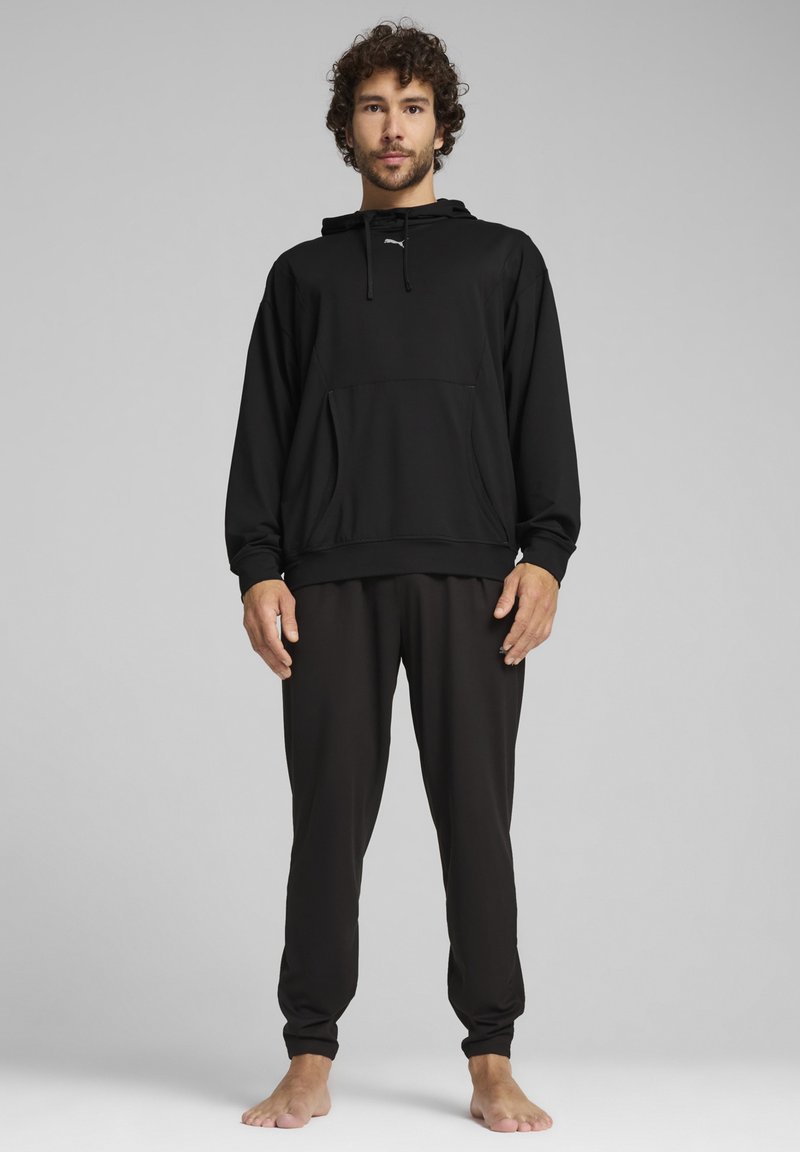 Haut à capuche noir avec cordon de serrage et poche avant, associé à un pantalon noir ajusté. Tissu doux et lisse avec une coupe ajustée.