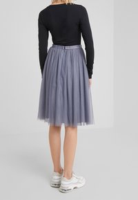 Gonna midi in tulle grigia con pois, caratterizzata da una vita aderente e un dettaglio con fiocco, abbinata a un top nero a maniche lunghe e sneakers bianche.