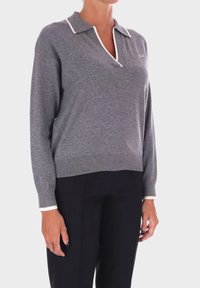 Pullover grigio a maglia con colletto polo, caratterizzato da cuciture bianche a contrasto e maniche lunghe. Indossato sopra pantaloni neri, con un orlo a coste.