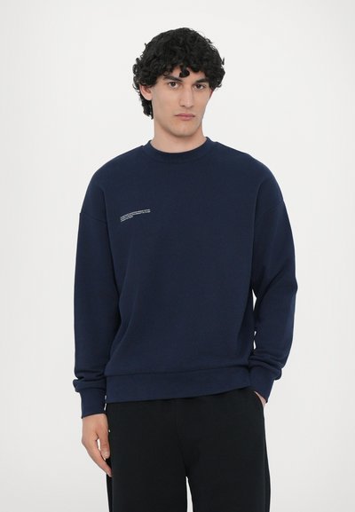 Marineblå sweatshirt i blødt stof med rund hals og dropped shoulders. Har diskret hvid tekstdetalje på brystet. Sammen med sorte bukser.