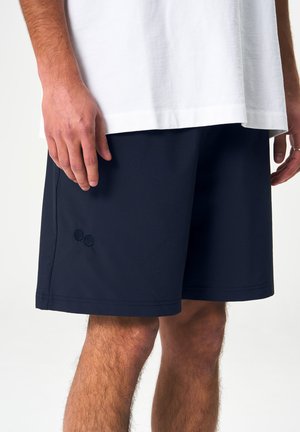 Dunkelmarinefarbene Shorts aus leichtem Material mit einem elastischen Bund. Mit zwei gestickten Kreisen am linken Oberschenkel.