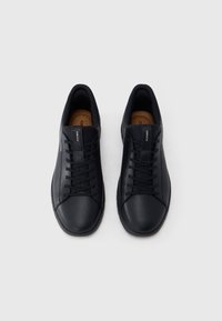 Ζευγάρι μαύρα δερμάτινα sneakers με κορδόνια, χαμηλή γραμμή και καφέ εσωτερικό, τοποθετημένα δίπλα-δίπλα σε λευκό φόντο.