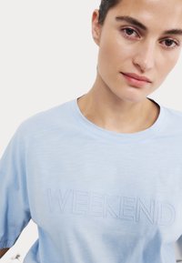 Camiseta de manga corta azul claro hecha de una tela suave, con un texto bordado "WEEKEND" en un tono ligeramente más oscuro.