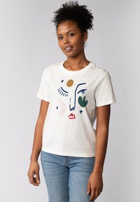 Witte t-shirt met korte mouwen, voorzien van een grafisch ontwerp van abstracte gezichtskenmerken in verschillende kleuren, waaronder blauw, rood, groen en bruin.