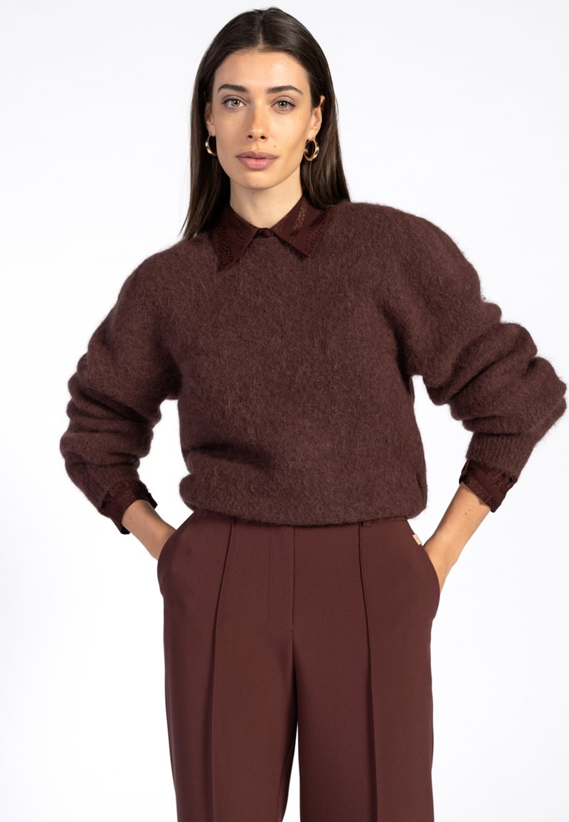 Bordeaux fuzzy trui met een ronde halslijn, drop shoulders en geribbelde manchetten, gelaagd over een bruine blouse met kraag. Op maat gemaakte bruine trousers.