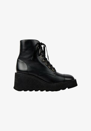 Bottine noire en cuir à lacets montant à la cheville avec semelle compensée épaisse et semelle rainurée, vue de profil sur fond blanc.