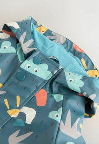 Impermeabile turchese con fantasie colorate di animali. Presenta un cappuccio foderato, bottoni a pressione e una finitura liscia e resistente all'acqua.