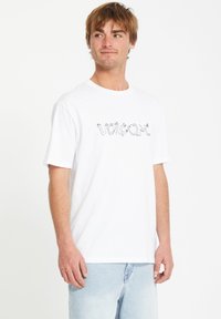 T-shirt en coton blanc avec un logo graphique noir "Volcom", manches courtes et col rond. Coupe décontractée avec une texture douce.