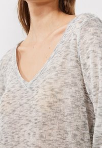 V-Ausschnitt-Pullover in Hellgrau mit einem gesprenkelten Muster, aus leichtem, strukturiertem Strick und mit leicht lockerer Passform.