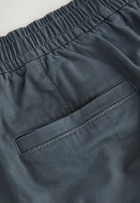 Sötétkék anyagú sort, amely elasztikus derékrésszel, sima textúrával és egy hátsó zsebbel rendelkezik, finom varrási részletekkel.