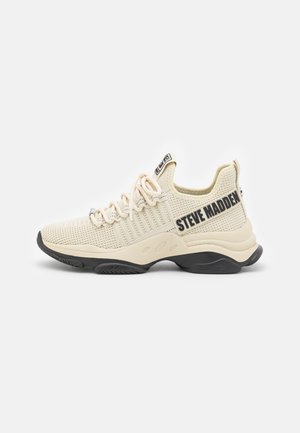 Beżowy sneaker z siateczki z grubą czarną podeszwą, sznurowany z przodu i dużym napisem "Steve Madden" na boku.