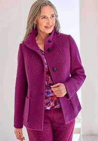 Getailleerde paarse wolmix jas met een kraag, knoopsluiting en twee zijzakken. Gedragen over een gestreepte top en bijpassende broek.