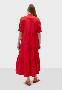 Robe maxi en coton rouge avec des manches courtes, volants en couches et coupe décontractée, accompagnée de sandales rouges simples.