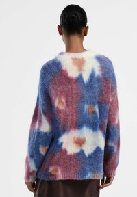 Maglione oversize multicolore con una consistenza morbida e pelosa in tonalità di blu, rosa e crema, con motivi astratti.