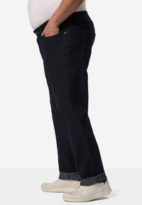 Jeans de mezclilla azul oscuro con un corte relajado, que cuentan con un bolsillo frontal, un ligero desgaste y puños enrollados. Combinados con zapatillas deportivas de color claro.