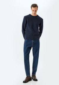 Marineblauer Strickpullover mit einem strukturierten Muster, kombiniert mit hellblauen Jeans und dunkelbraunen Stiefeletten. Einfaches, lässiges Outfit.