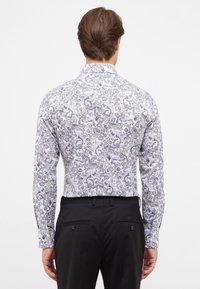 Langsleeveshirt met een zwart-wit ingewikkeld bloem- en diertjespatroon, met een klassieke kraag en knoopmanchetten, gedragen met zwarte broek.