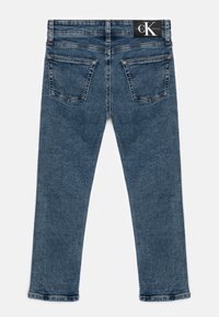 Jeans in denim blu scuro con design a gamba dritta, cinque tasche e cuciture a contrasto. Presentano un'etichetta del logo Calvin Klein nera in vita.