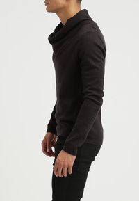 Mörkgrå sweatshirt med huva och långa ärmar. Mjukt tyg med texturerad yta. Figurformad silhuett, bärs med svarta byxor. Sidsyn.