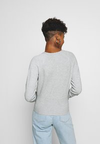 Maglione lavorato a maglia grigio chiaro con scollo rotondo e orlo a costine. La texture appare morbida, con maniche lunghe e una vestibilità aderente in vita.
