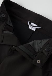 Zwarte broek met een tailleband met knoop, ritssluiting, verstelbare band en zichtbaar etiket aan de binnenkant.