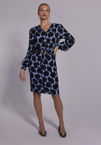 Czarna i niebieska sukienka w wzory z dekoltem w serek oraz długimi, bufiastymi rękawami, ściągnięta w talii paskiem z okrągłą klamrą.