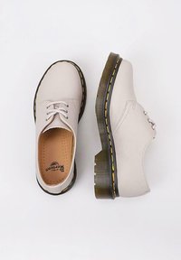 Scarpe in pelle grigia chiara con punta rotonda, caratterizzate da una texture impressa, lacci bianchi e un dettaglio di cucitura gialla a contrasto lungo la suola.