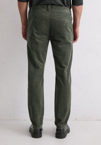Grüne Cordhose von hinten betrachtet, mit geradem Bein, zwei Gesäßtaschen und schwarzem Schuhwerk mit dicker Sohle.