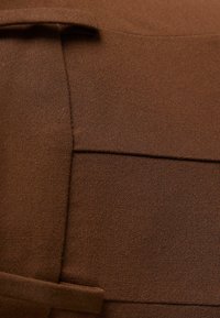 Brunt tyg med en strukturerad, vävd yta har en framträdande söm och en platt del som sträcker sig ut likt ett band eller flik.