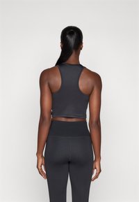 Top sportivo nero a crop con design racerback, forma aderente e texture liscia, abbinato a leggings neri a vita alta.