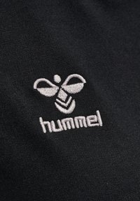 Svart tyg med en slät textur som har en vit broderad logotyp av en stiliserad bi ovanför ordet "hummel" i vit tråd.