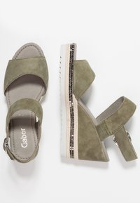 Olivgröna mocka kilsandaler med justerbart ankelsnöre, med en strukturerad vit sula och en metallisk detalj på kilen.