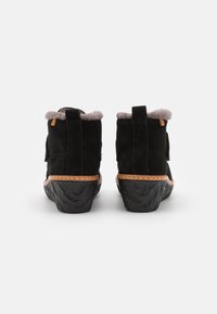 Black suede ankle boots with a soft grey fur lining, featuring a textured black rubber sole and a contrasting brown leather accent at the heel.