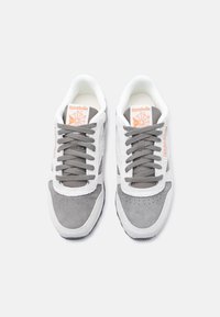 Ζευγάρι γκρι και λευκά αθλητικά παπούτσια Reebok με γκρι κορδόνια και πορτοκαλί λογότυπο στη γλώσσα και στο πλάι, σε λευκό φόντο, από πάνω.